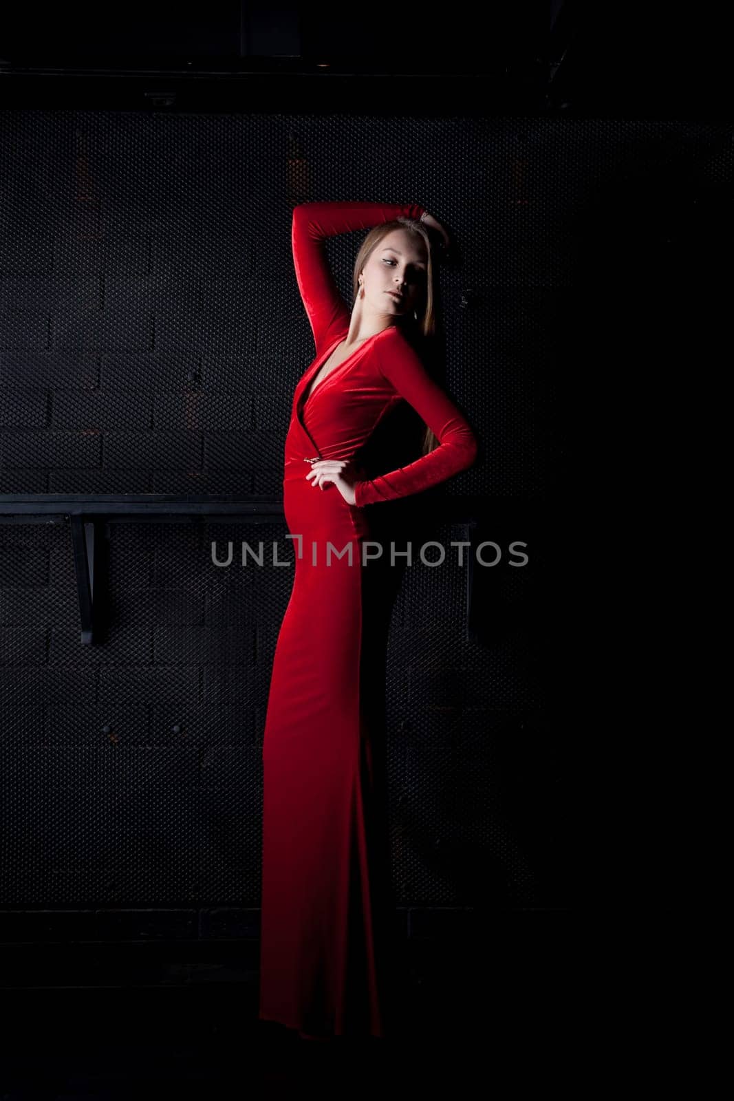 Full length portrait of beautiful woman in red long dress in dark club