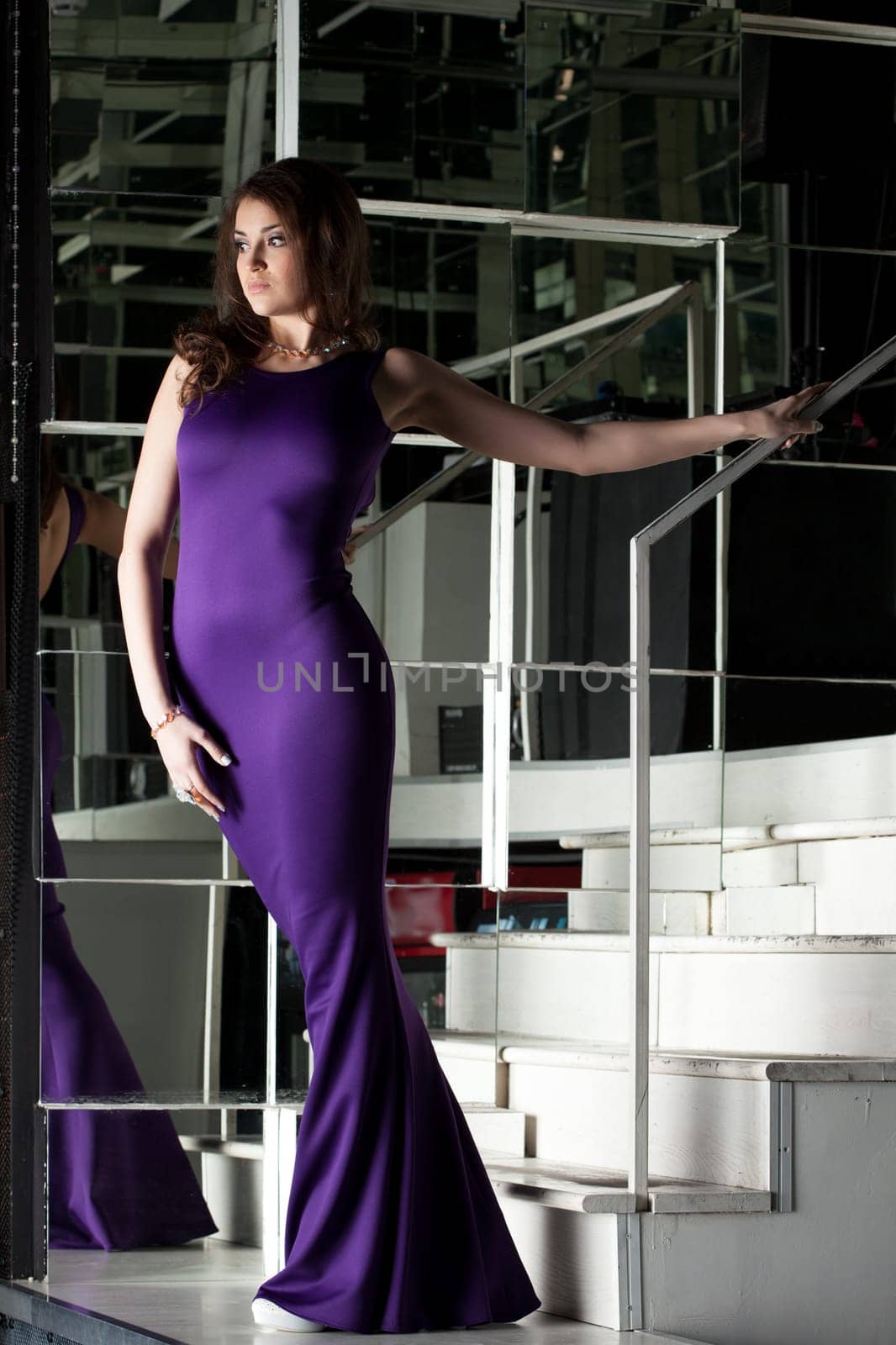 Full length portrait of pretty brunette woman in long purple dress posing on stairs
