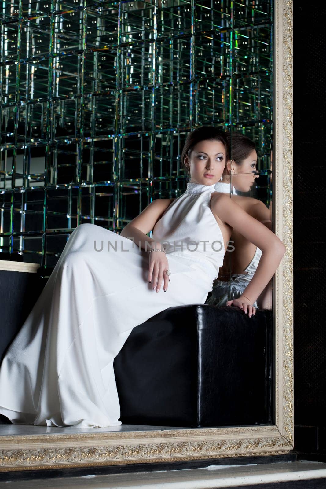 Full length portrait of brunette woman in white dress sitting on sofa