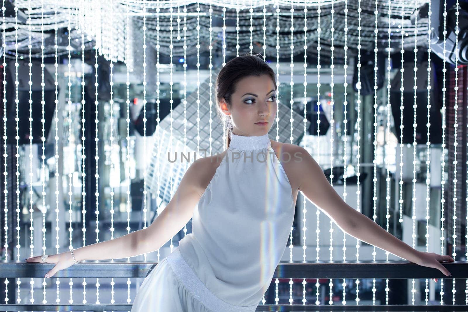 Glamour portrait of young woman in long white dress posing in night club