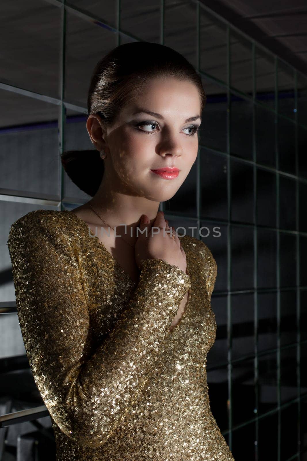 Portrait of brunette woman in long gold dress sitting on sofa near mirror