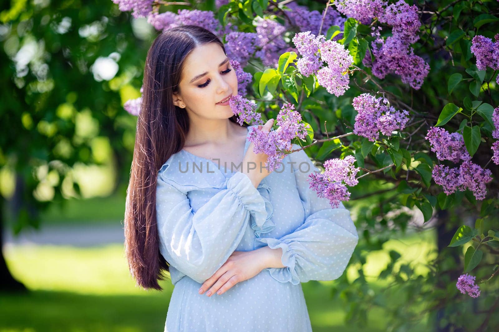 Pretty girl with long hair , in light blue dress stands with lilac flowers, in the garden, in sunny day. Close up. copy space