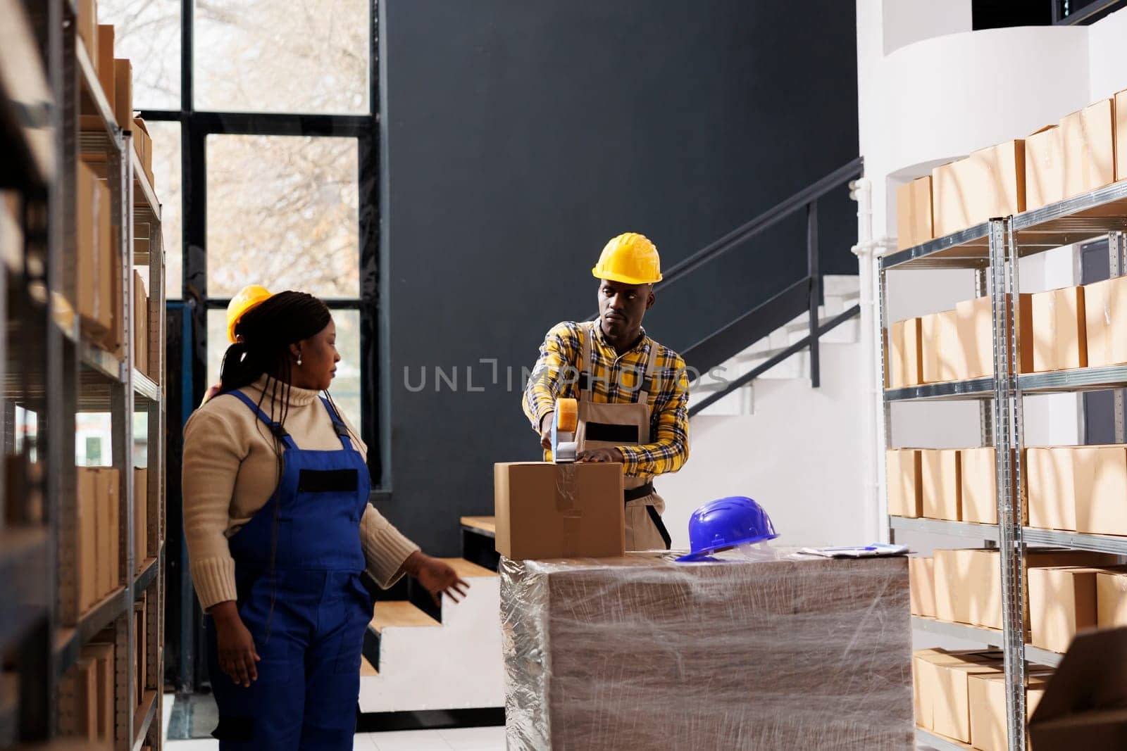 African american retail storehouse workers packing packages for shipment. All black delivery department employees team preparing parcels for transportation and using adhesive tape dispenser