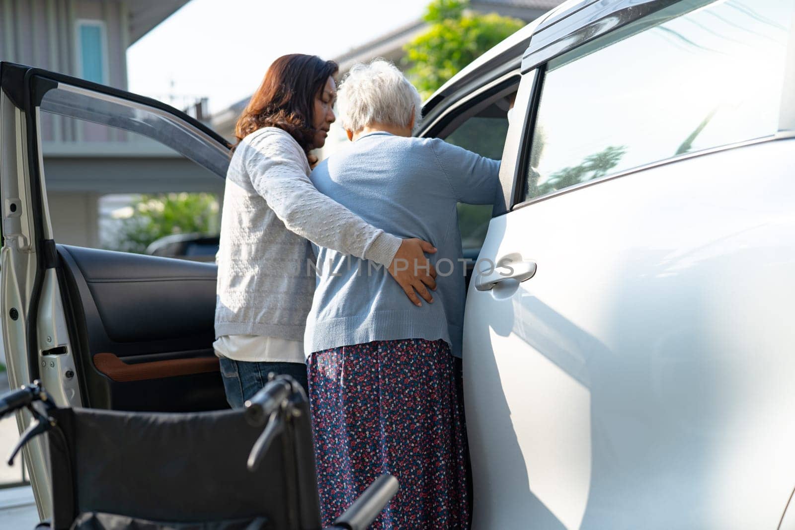 Caregiver help and support asian elderly woman sitting on wheelchair prepare get to her car to travel in holiday.