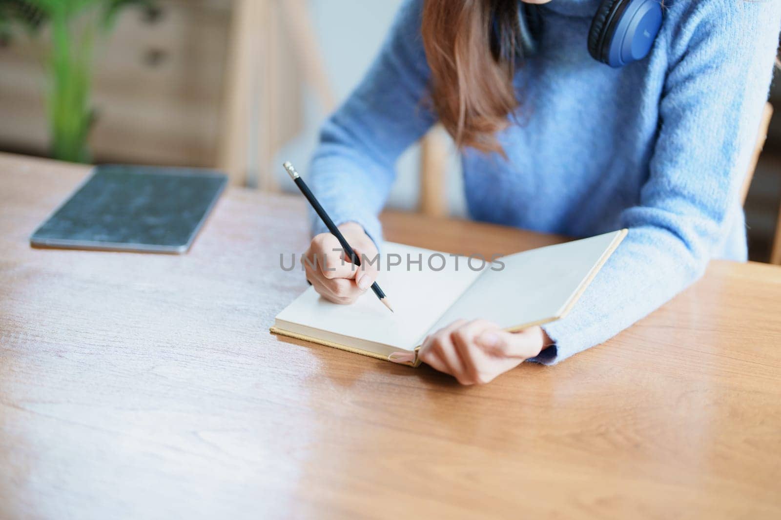 Portrait of a teenage Asian woman using a notebook to study online via video conferencing on a wooden desk at home by Manastrong