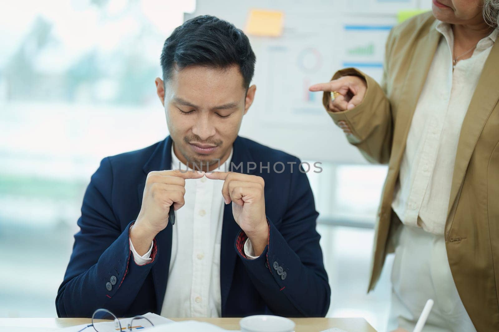 An image of an Asian male employee looking worried and sad about being scolded by his boss for failing to meet sales targets, concept of disappointment and failure in his career.