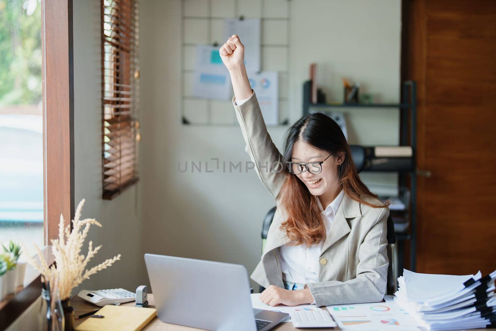 Portrait of a woman business owner showing a happy smiling face as he has successfully invested her business using computers and financial budget documents at work.