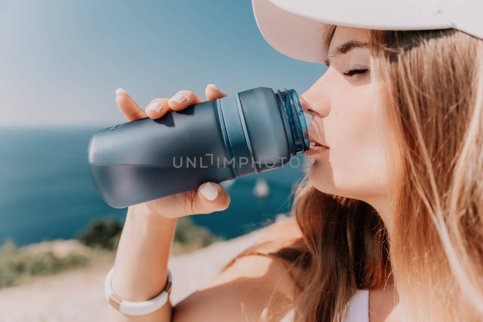 Fintess woman drinking water. Happy, active middle aged woman standing on beach and drinking water after excersise. Concept of lifestyle, sport. Close up by panophotograph