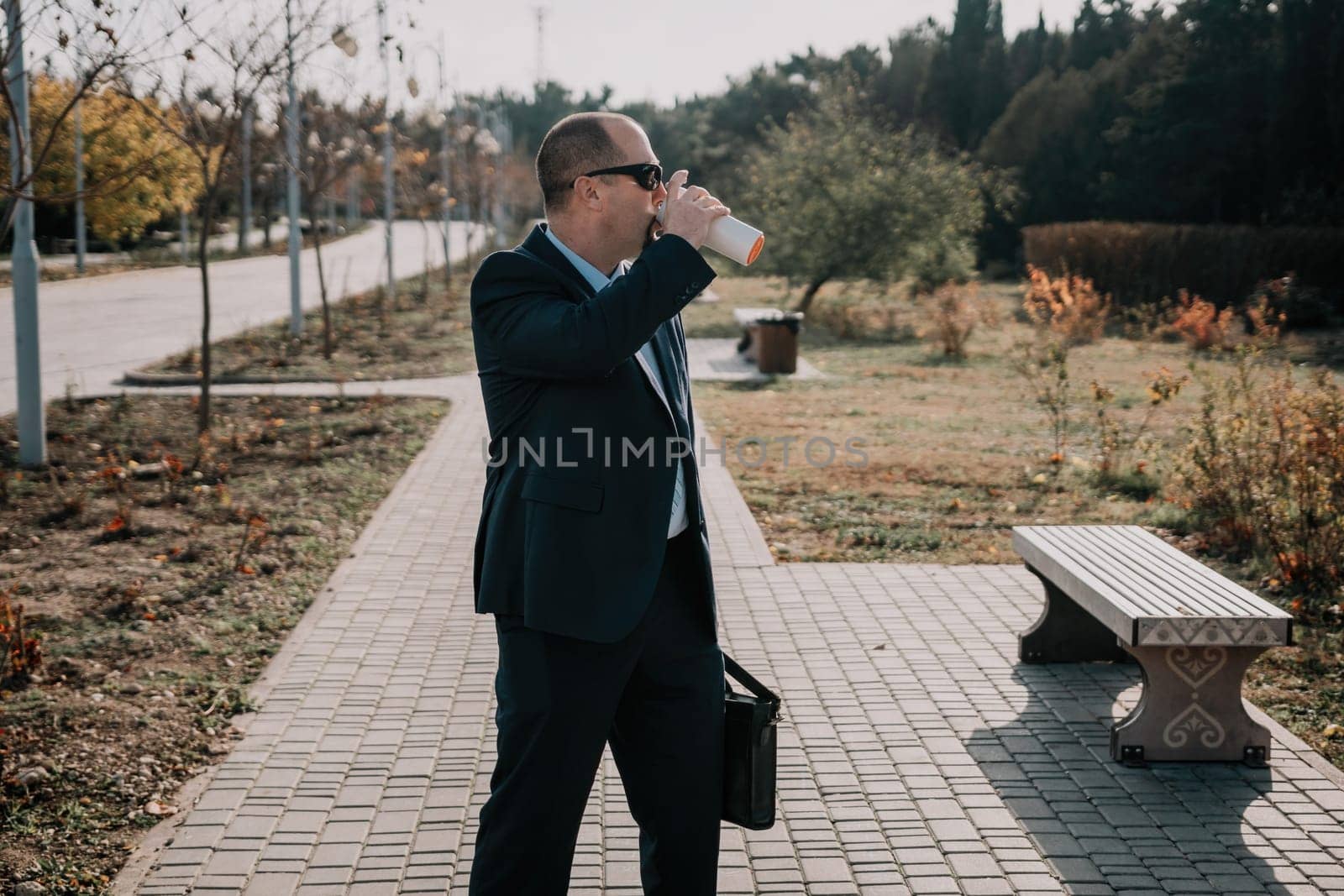 Mature entrepreneur drink coffee in autumn park. Senior executive rest in city park. by panophotograph