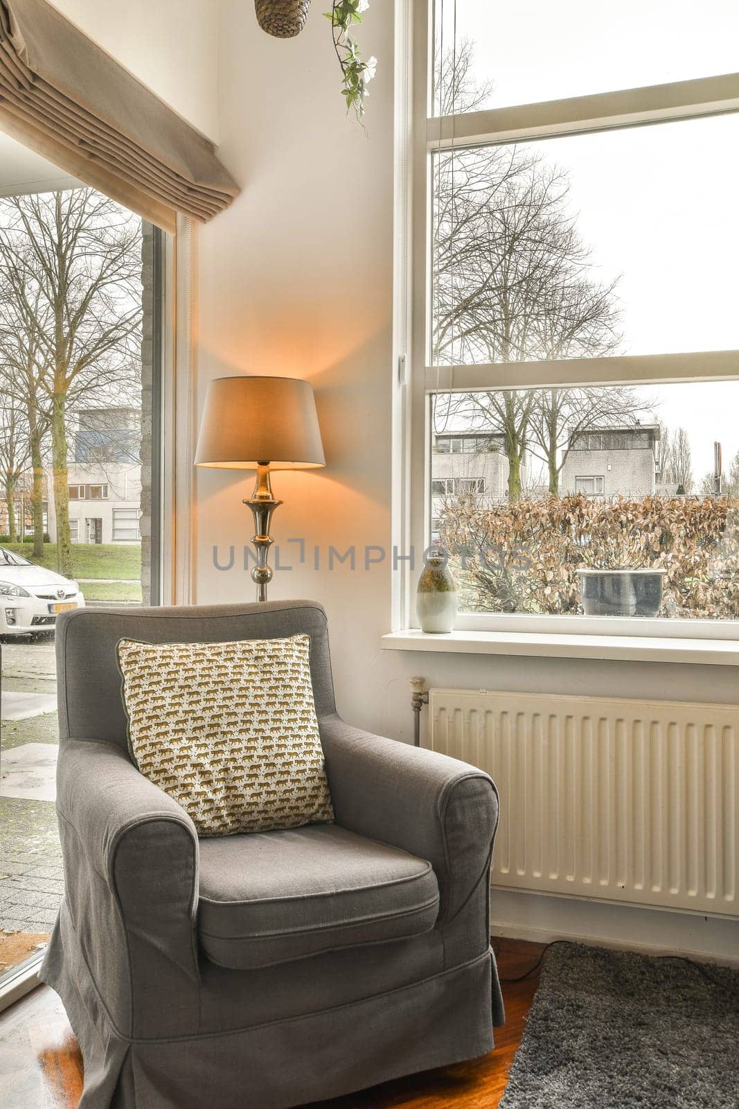 a living room with a chair, lamp and large window looking out onto the street in front of the house