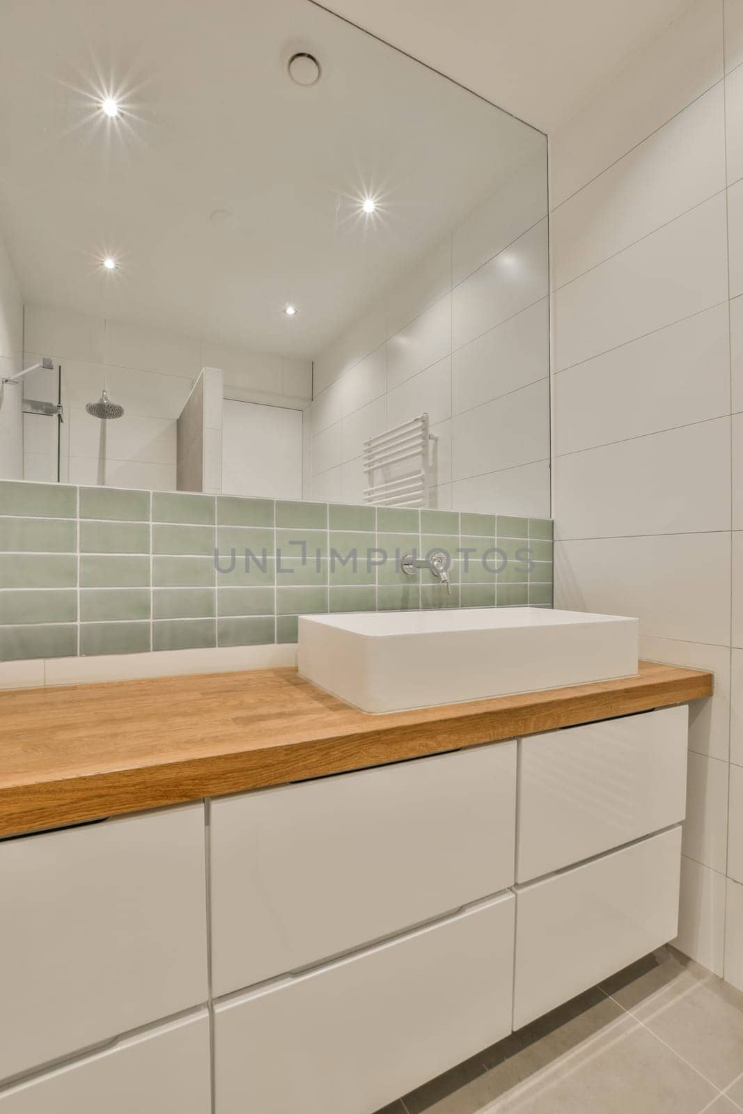 a modern bathroom with white cabinets and green tiles on the wall behind it is a large mirror above the sink