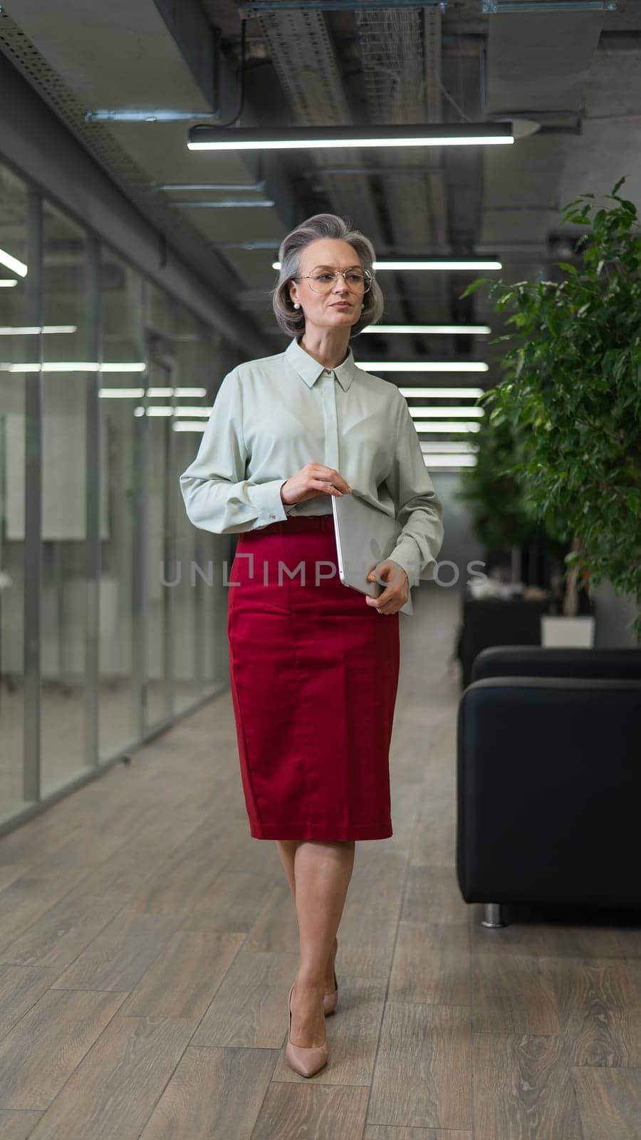 Attractive mature caucasian woman holding laptop while standing in office