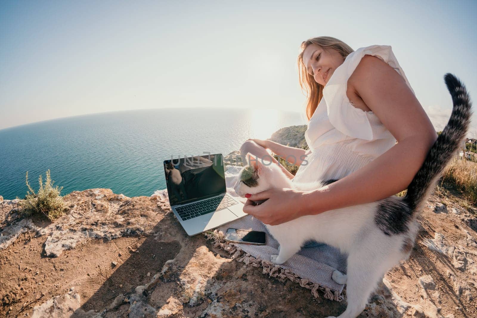 Woman sea laptop. Business woman petting cat and working on laptop by the sea. Close up on hands of pretty lady typing on computer outdoors summer day. Freelance, digital nomad and holidays concept. by panophotograph