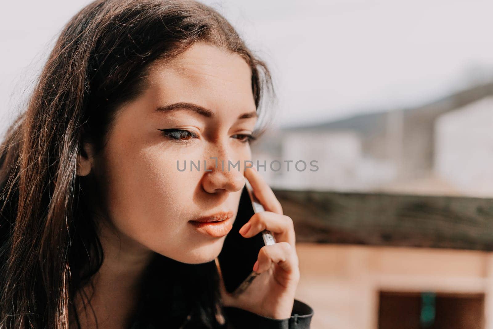 Happy young smiling woman with freckles outdoors portrait. Soft sunny colors. Outdoor close-up portrait of a young brunette woman and looking to the camera, posing against nature background.