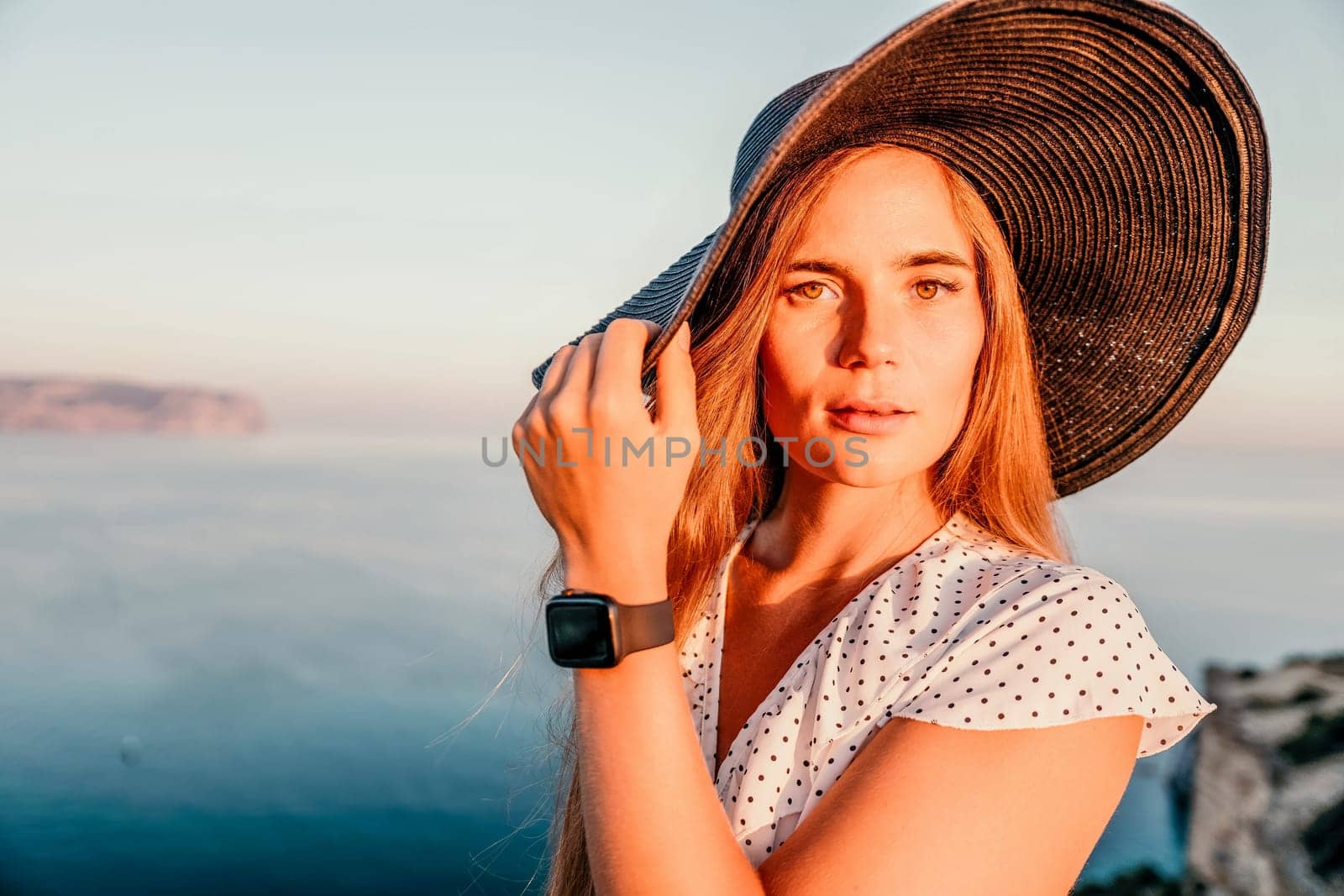 Portrait of happy young woman wearing summer black hat with large brim at beach on sunset. Closeup face of attractive girl with black straw hat. Happy young woman smiling and looking at camera at sea