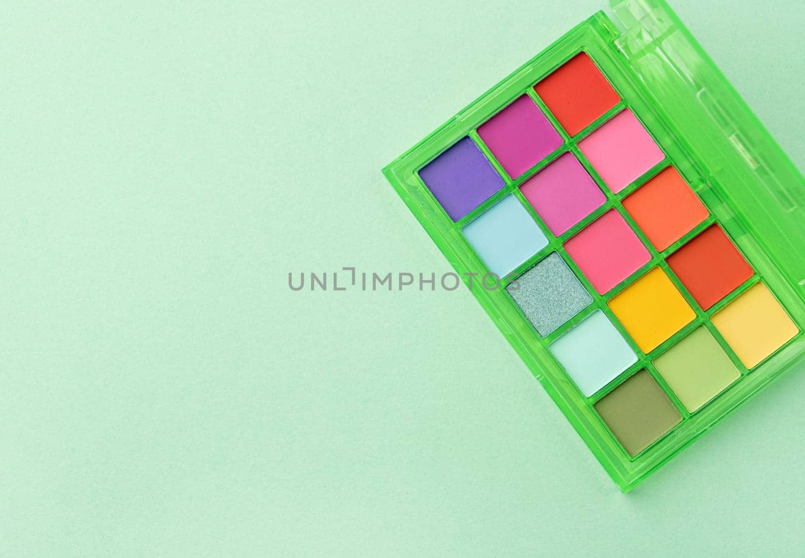 Bright summer eyeshadow palette and makeup products in pink cosmetic bag on green background. Makeup cosmetics. Colorful colors. Place for text. Flat lay. Top view. layout