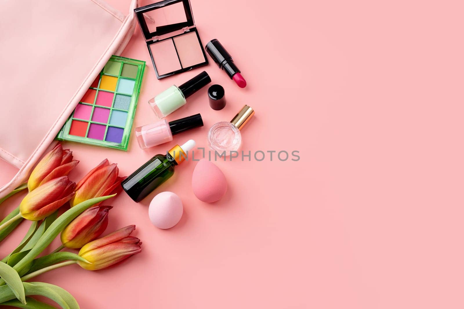 Bright summer eyeshadow palette and makeup products in pink cosmetic bag on green background. Makeup cosmetics. Colorful colors. Place for text. Flat lay. Top view. layout