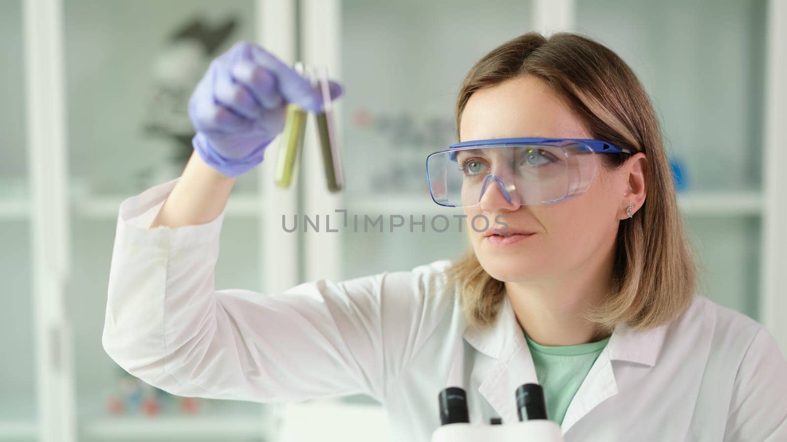 Woman chemist in protective glasses holding test tubes with liquid in hands in laboratory. Pharmaceutical business concept