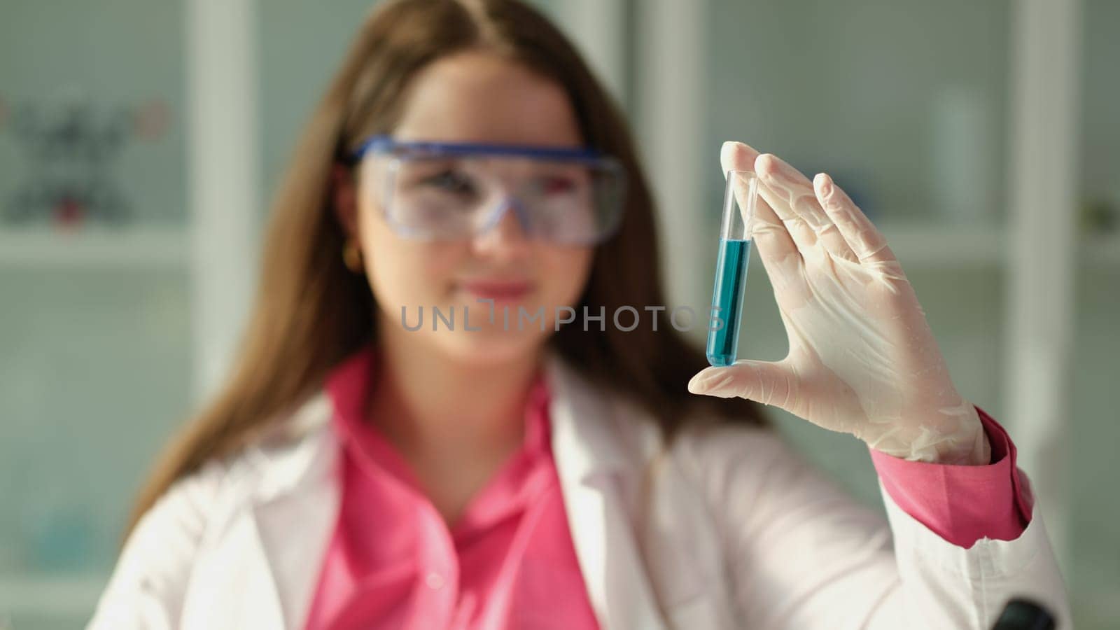 Woman scientist chemist holding test tube with blue liquid in chemical laboratory closeup. Production of detergents and cosmetics concept