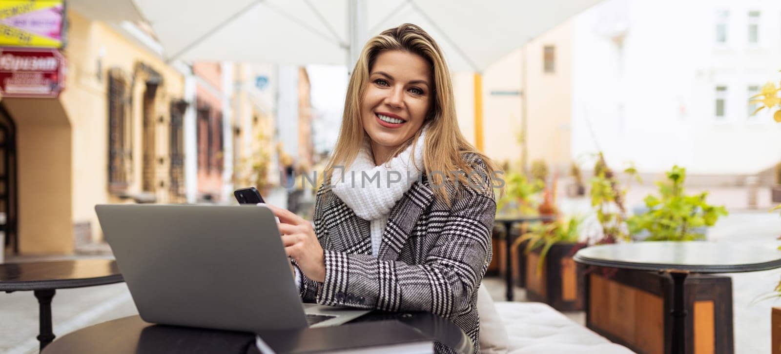 young blond woman journalist with a laptop sits on the terrace in a cafe.