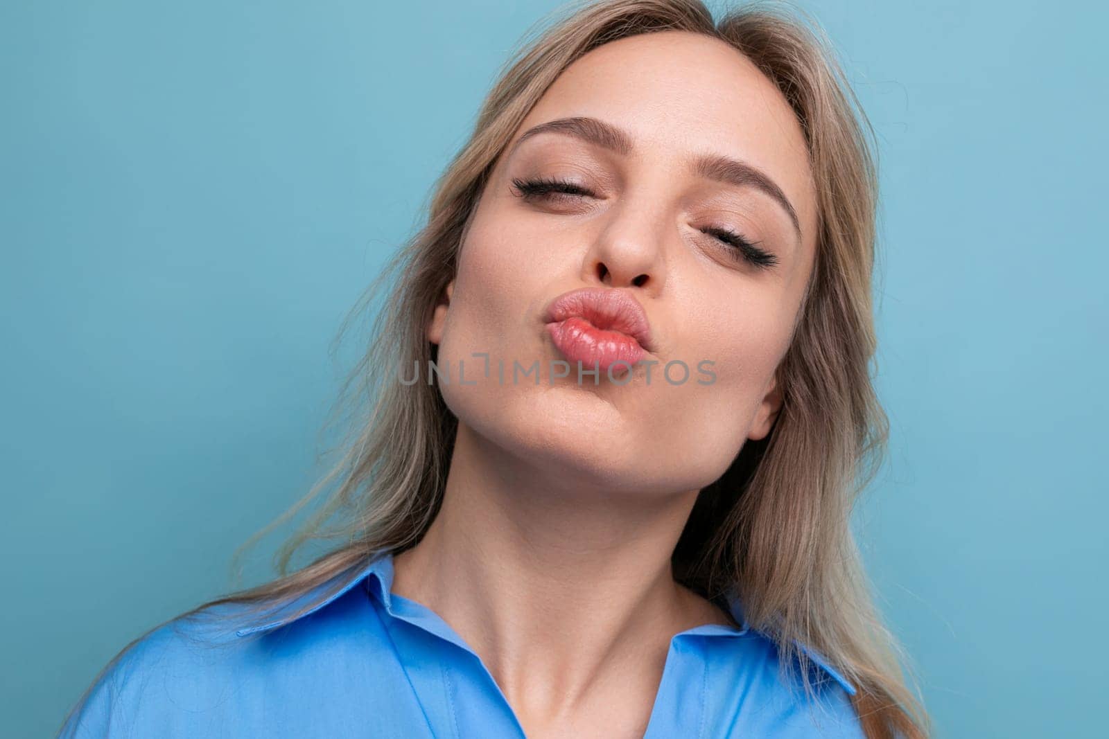 look of a happy European well-groomed blond girl sending a kiss on a blue background.