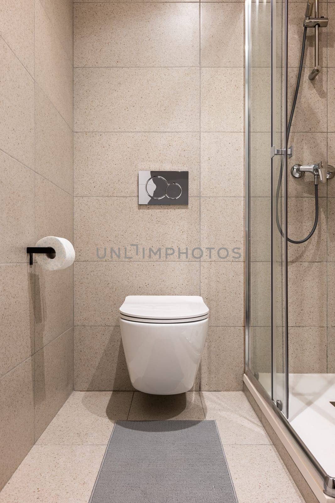 Direct shot of small bathroom with white wall-hung toilet and a glass shower with stylish beige tiles. Concept of a stylish but simple and concise design in the bathroom by apavlin