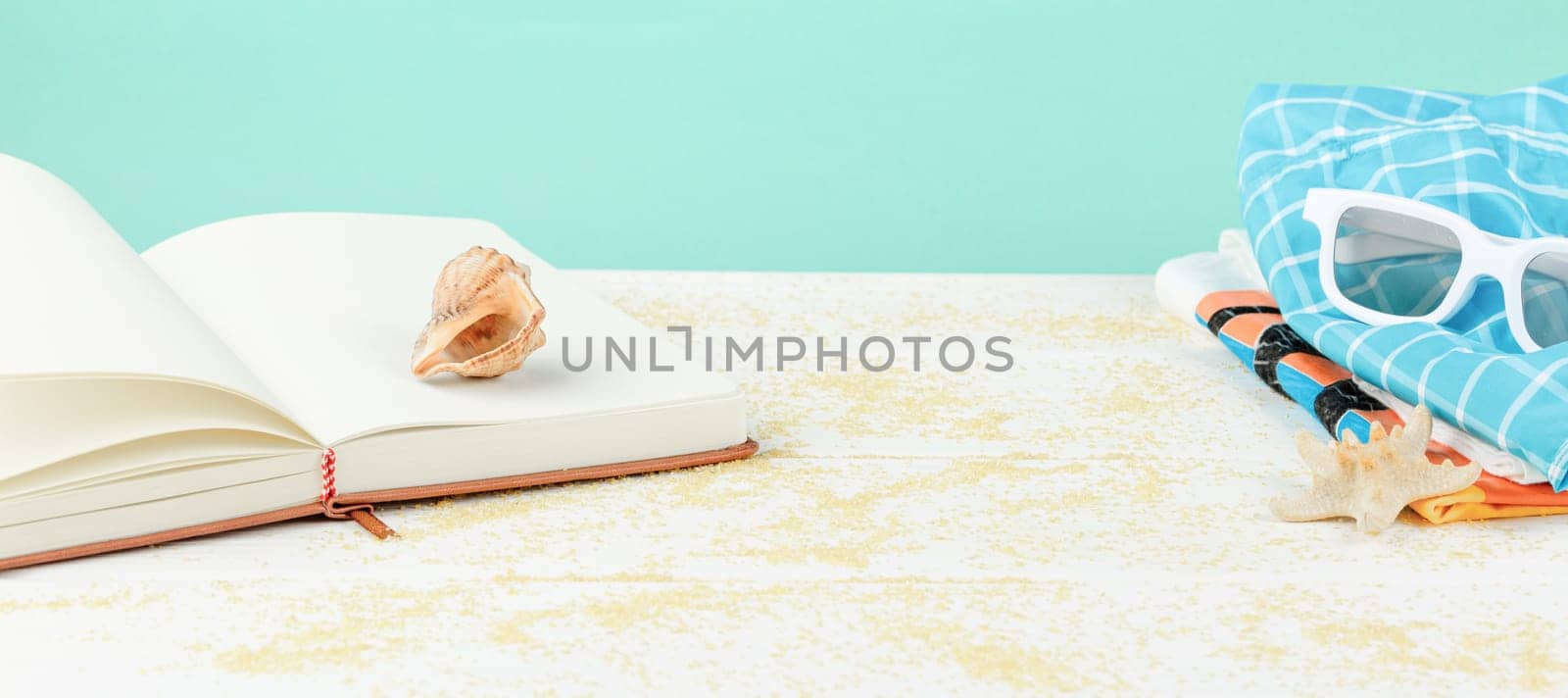 Summer time on the beach. Sunglasses with a book on a white wooden table. Sea vacation concept. Starfish and seashells on a sandy background.