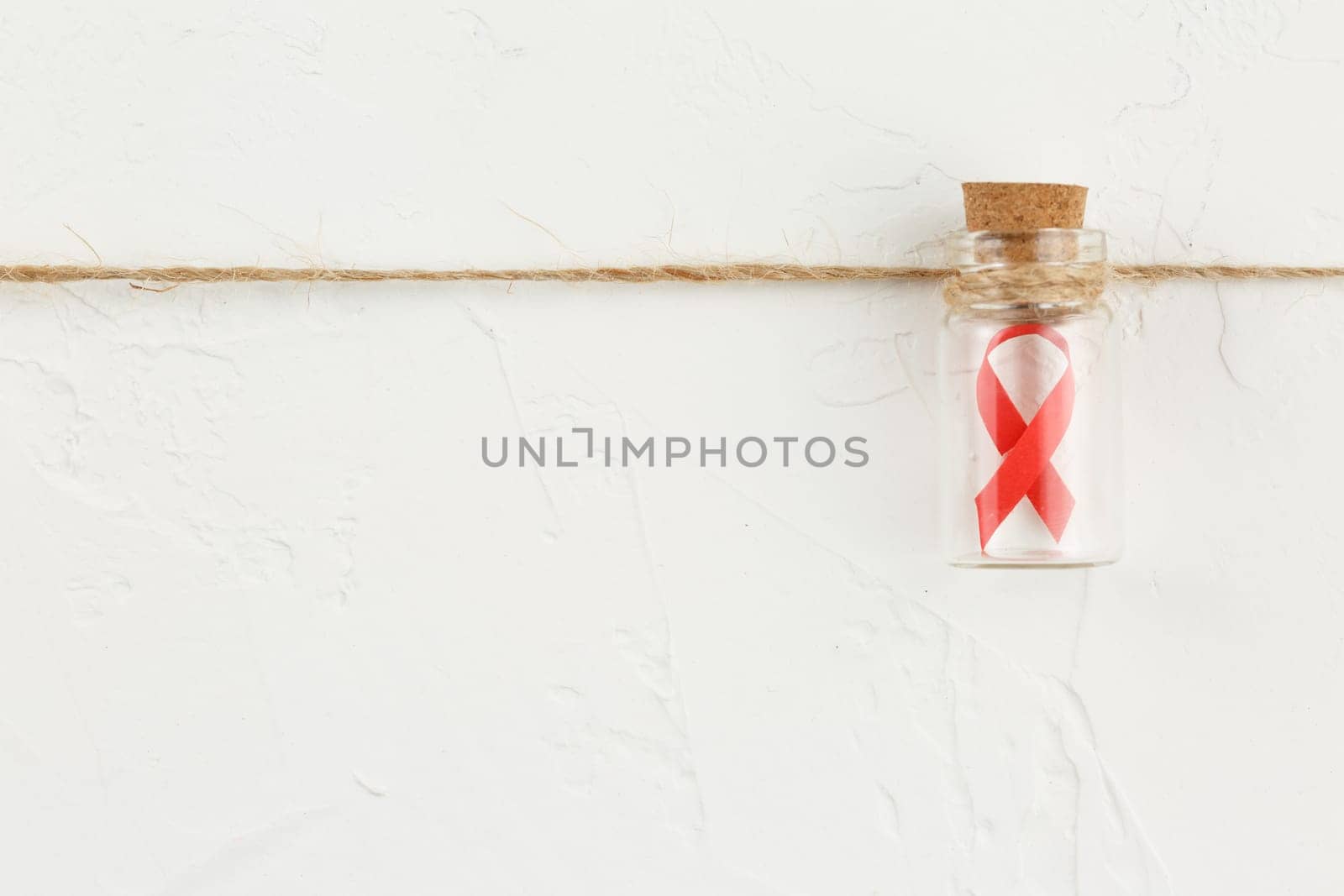 Red ribbon in a glass bottle with black notebook on white grunge background. Top view. Health care. AIDS prevention concept. Hiv and cancer awareness. Flat lay.