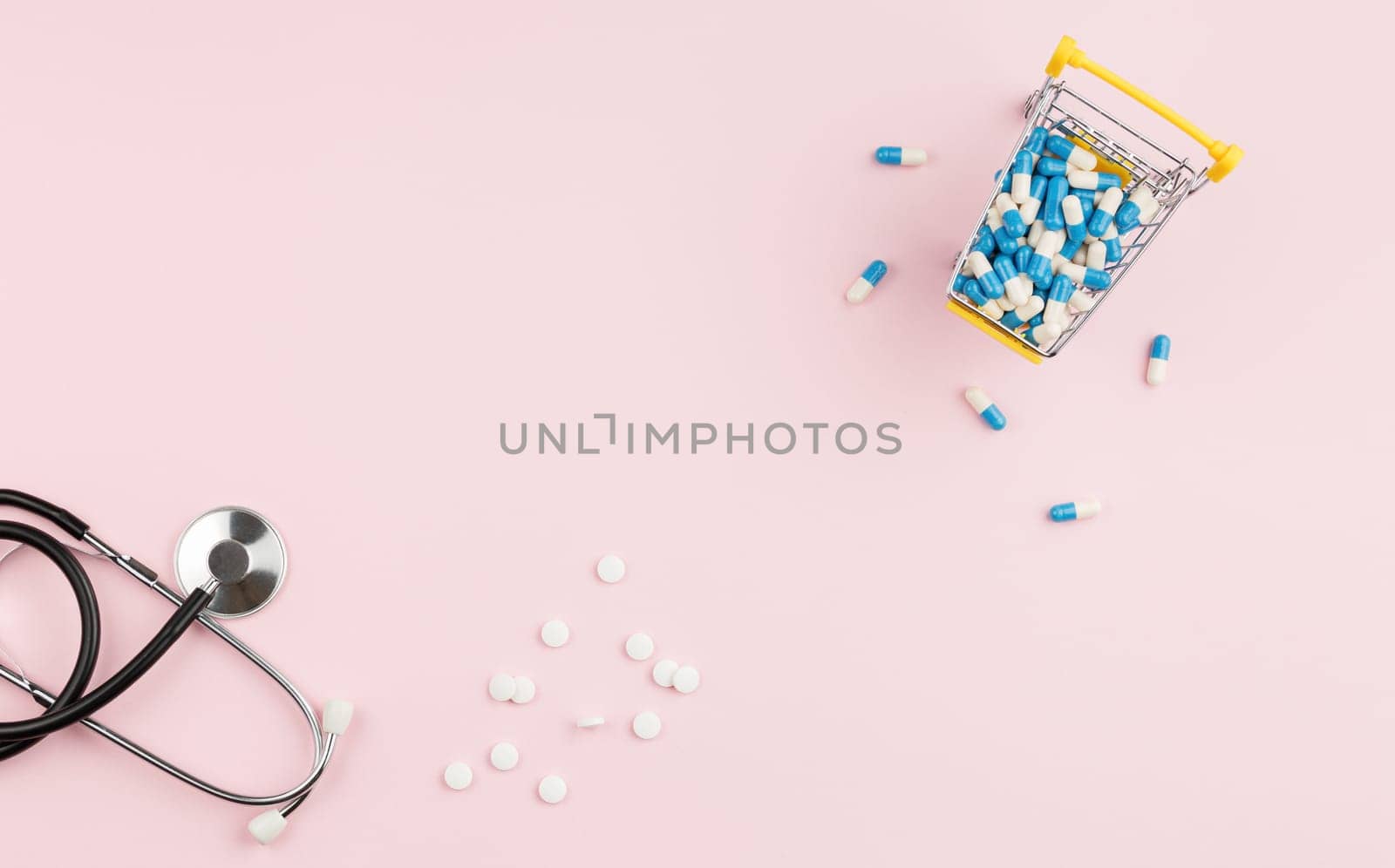 Supermarket trolley filled with pills on a pink background. Top view. Pharmacy concept. Stethoscope on the doctor table.