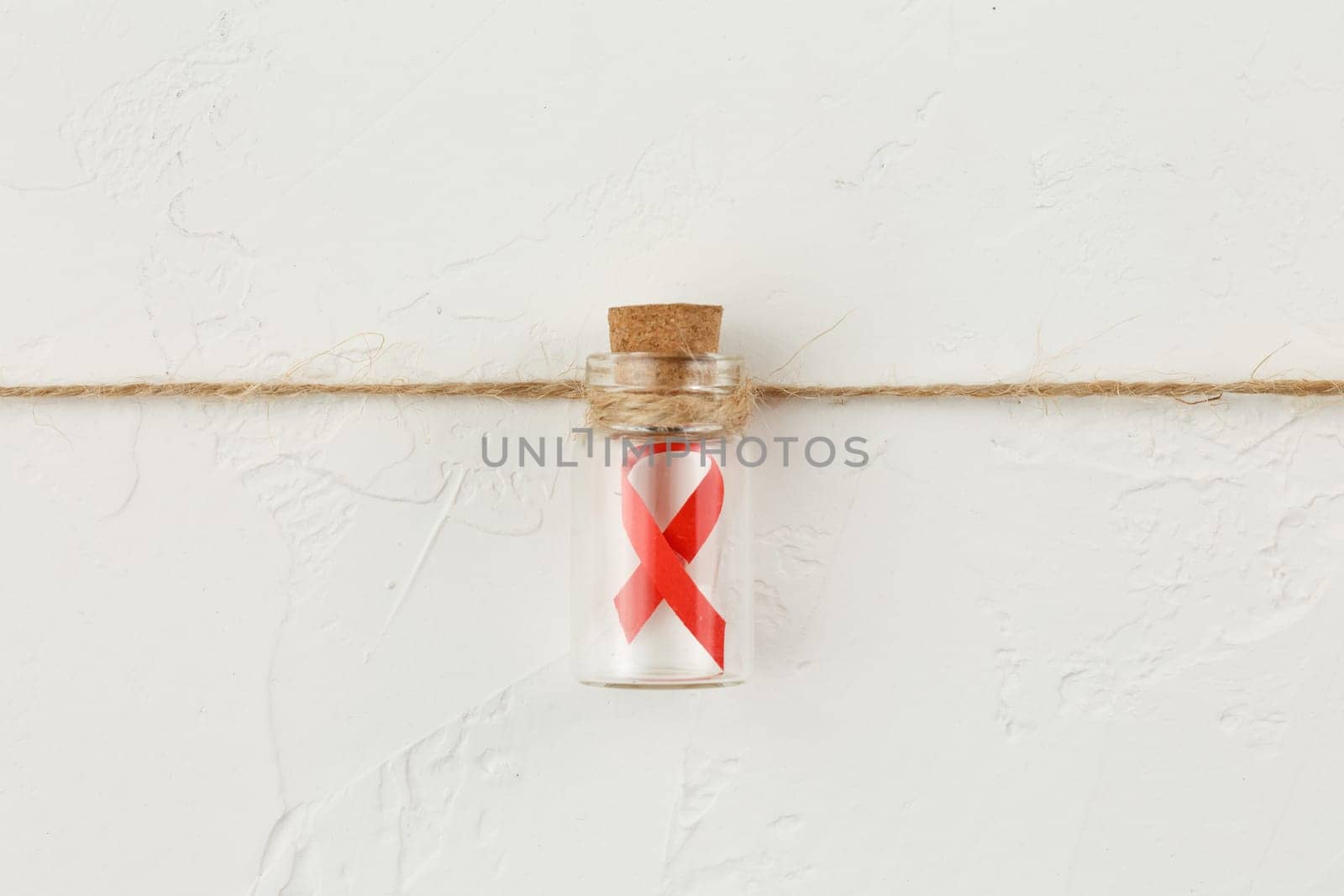 Red ribbon in a glass bottle on white grunge background. Top view. Health care. AIDS prevention concept. Hiv and cancer awareness. Flat lay.
