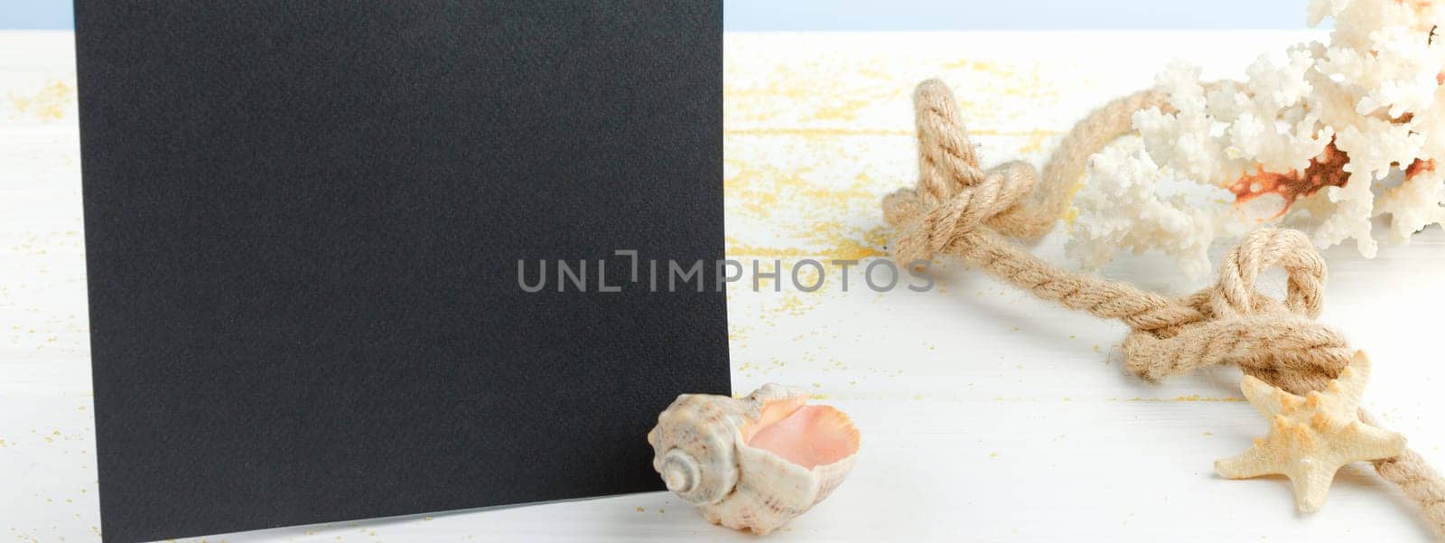 Black board on white wooden table with copyspace. Starfish and seashells with rope. Beach service banner.