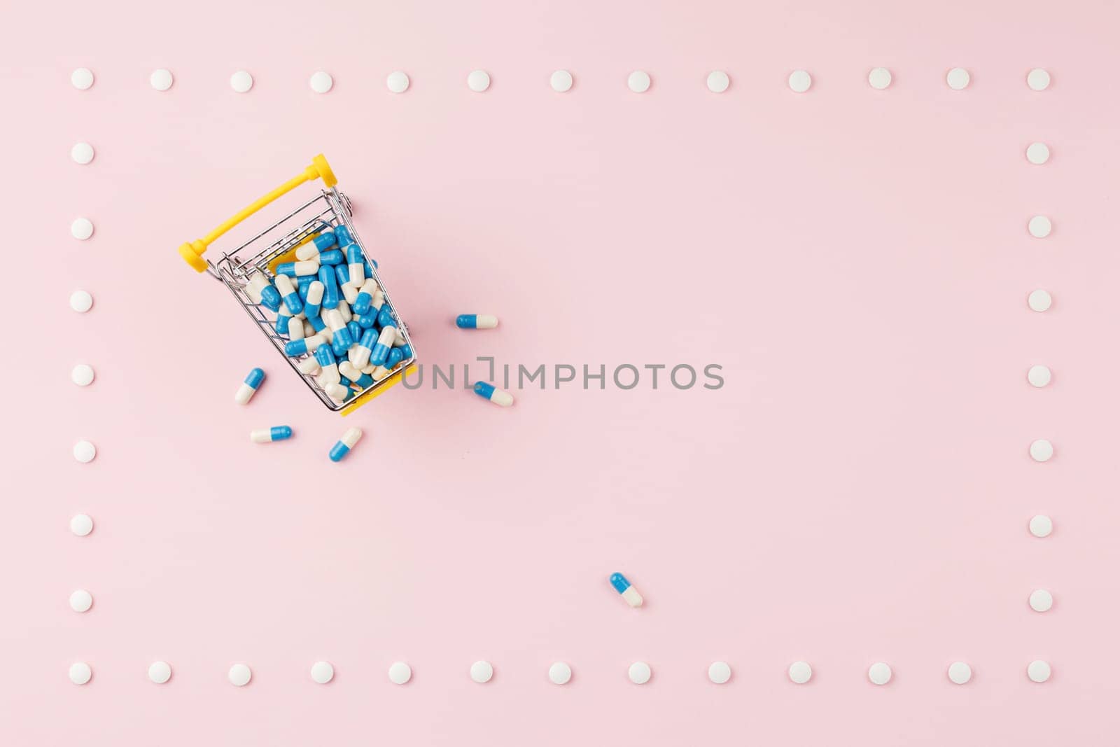 Supermarket trolley filled with capsules in a frame of pills on a pink background. Top view. Pharmacy concept.