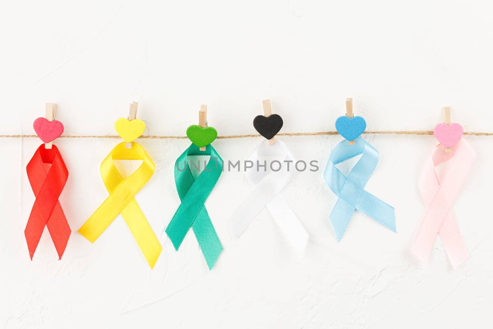 Colored ribbons on a rope with wooden clothespins with multicolored hearts against white background. Top view. Health care. AIDS prevention concept. Hiv and cancer awareness. Flat lay.