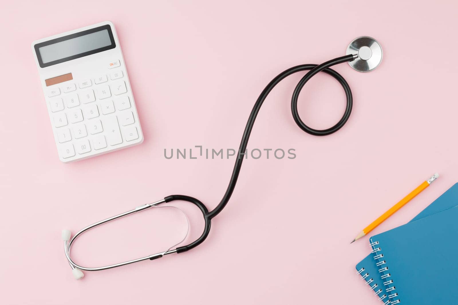 Calculator with a stethoscope on a pink table. by alexxndr