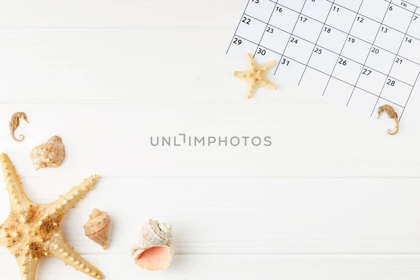 Summer vacation calendar at the sea on a white wooden background. Summer holiday concept. Decoration of starfish and seashells. Top view.