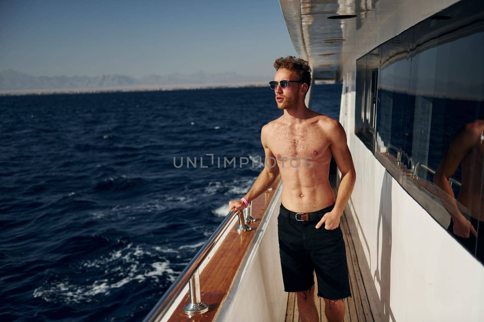 Warm weather. Young male tourist is on the yacht on the sea. Conception of vacation by Standret