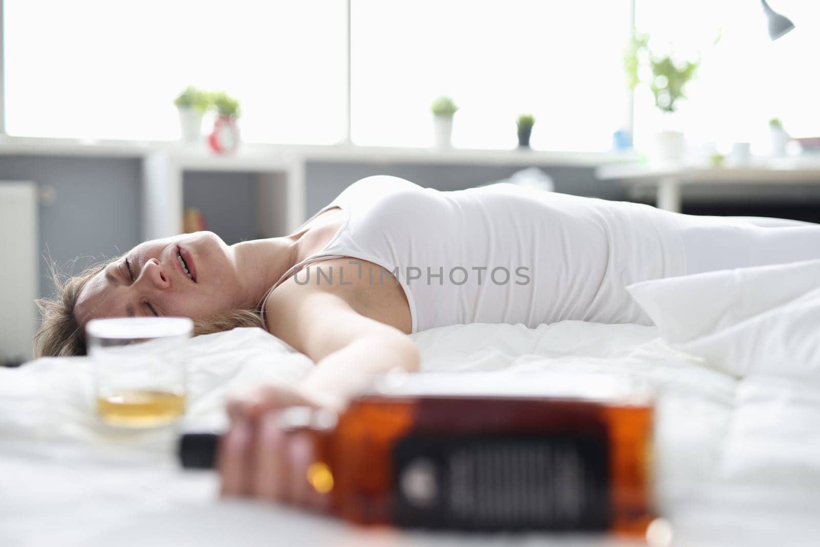 Drunk woman is sleeping on bed with bottle of alcohol. Female alcoholism and consequences of party concept