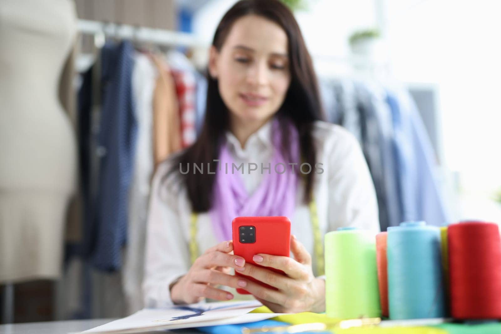 Woman seamstress stylist holding smartphone in atelier by kuprevich