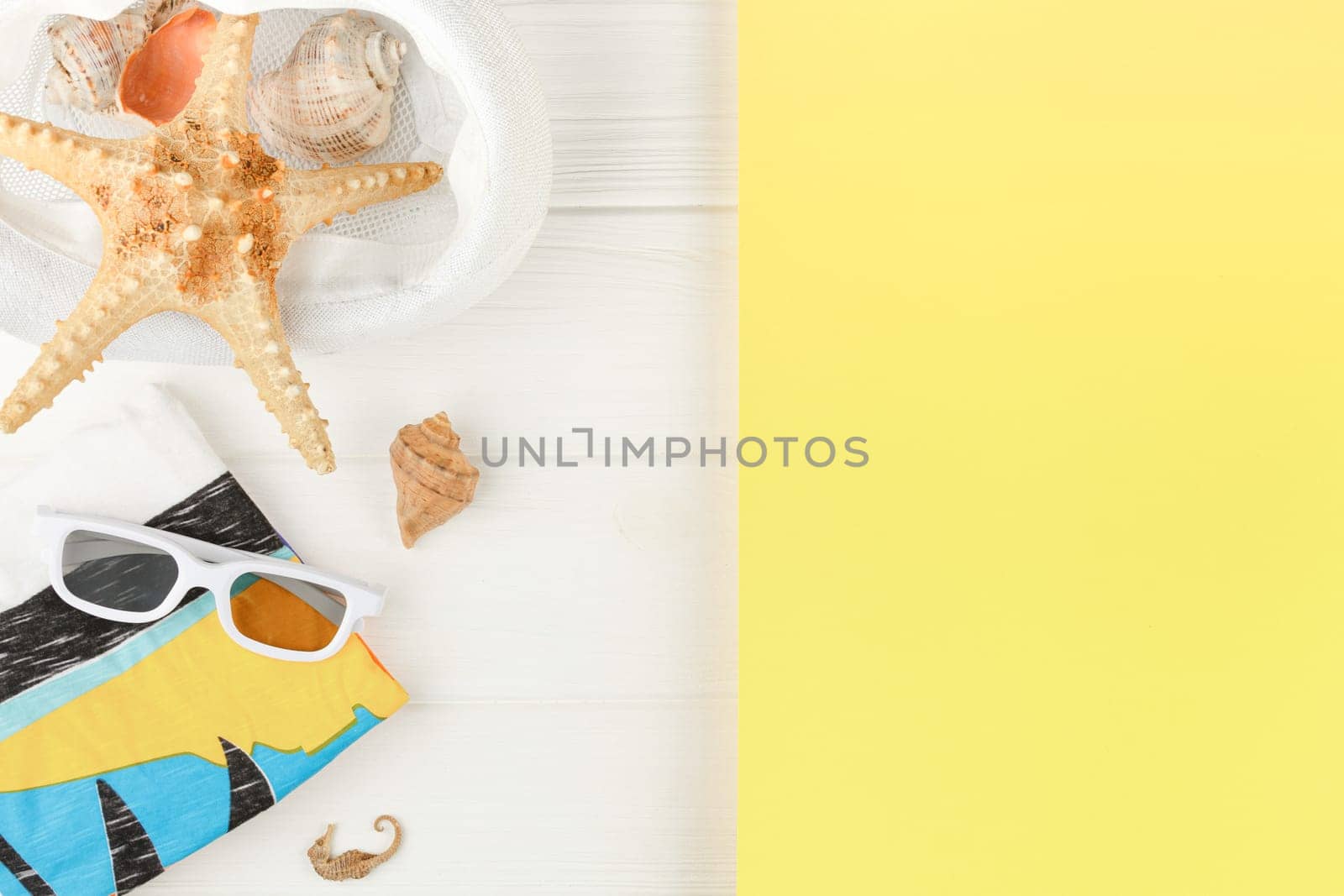 Beach hat with towel and sunglasses on white wooden background. Banner with yellow copy space. Summer vacation concept. Flat lay. Starfish and seashells Vertical photo.