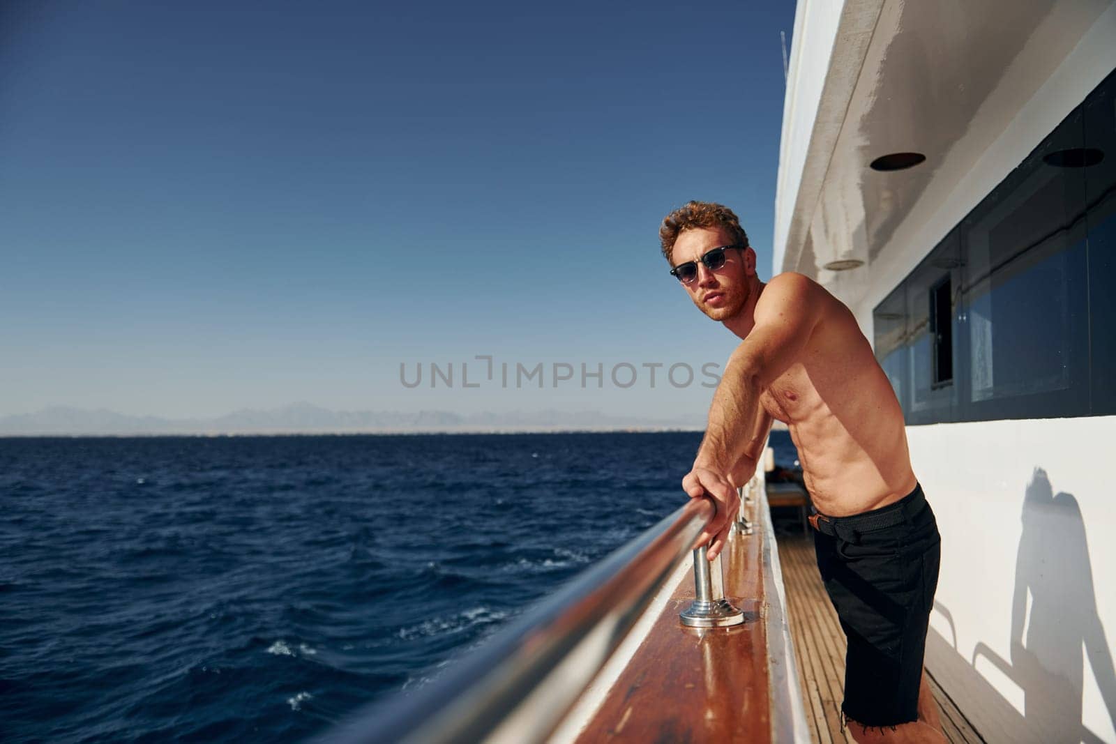Warm weather. Young male tourist is on the yacht on the sea. Conception of vacation.