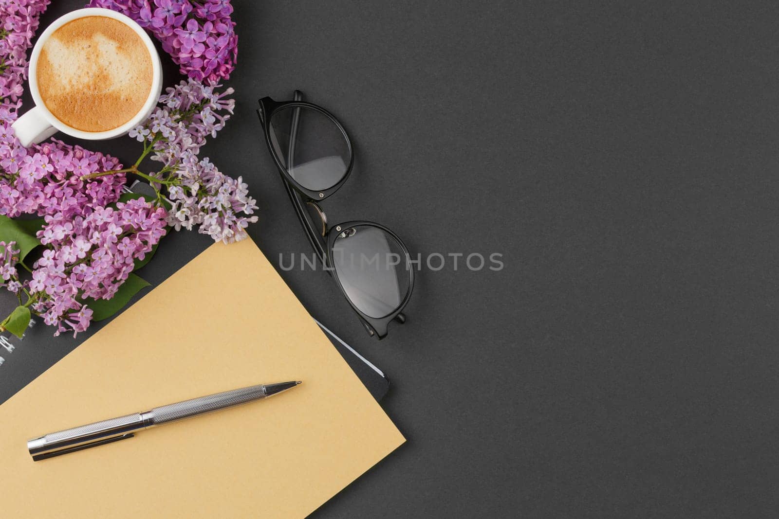 Spiral notebook with pen, glasses coffee cup and lilac flowers on an isolated background. Top view.