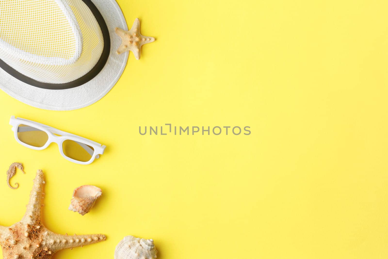 Summer hat with sunglasses on yellow isolated background. Flat lay. Beach vacation concept. Top view. Starfish and seashells.