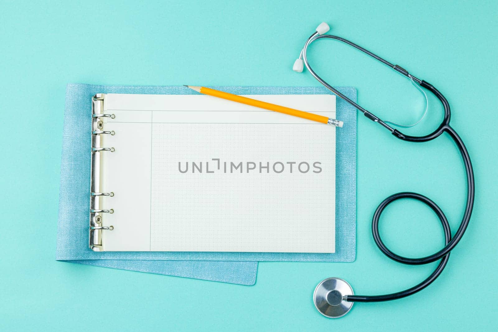 Stethoscope and open notepad in doctor office on green desk background top view. Nurse desktop concept.