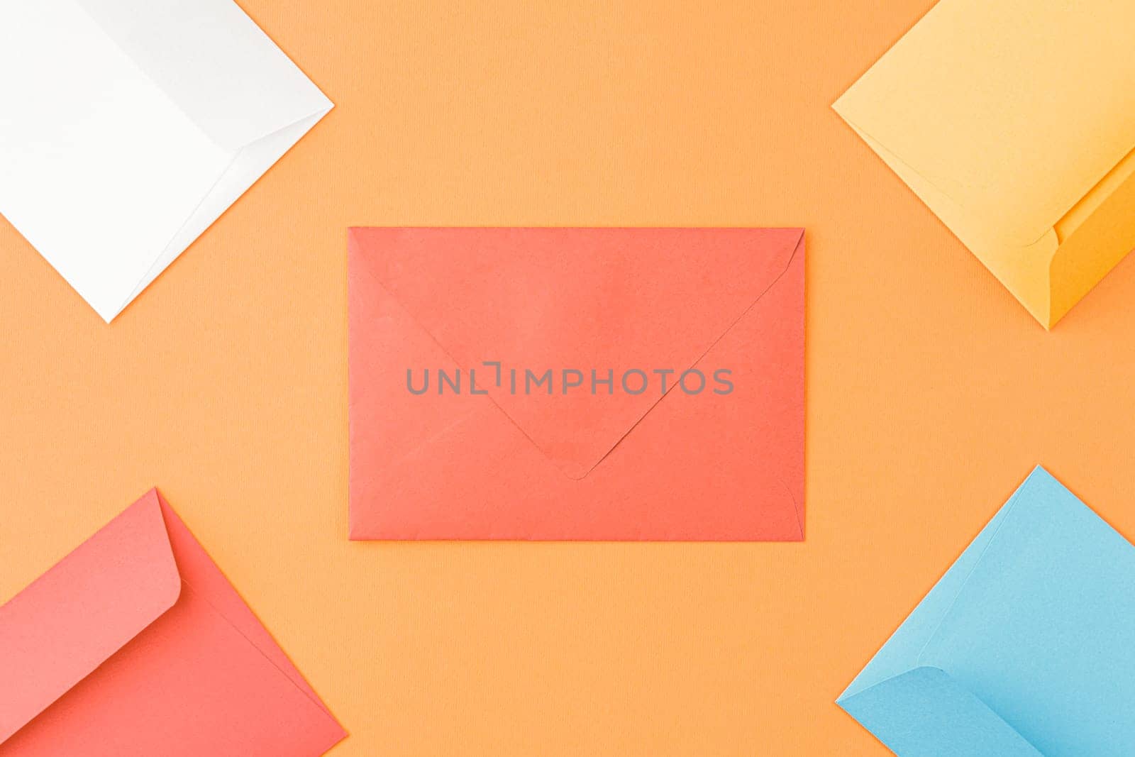 Multicolored paper mailing envelopes on orange isolated background. Top view, copy space.