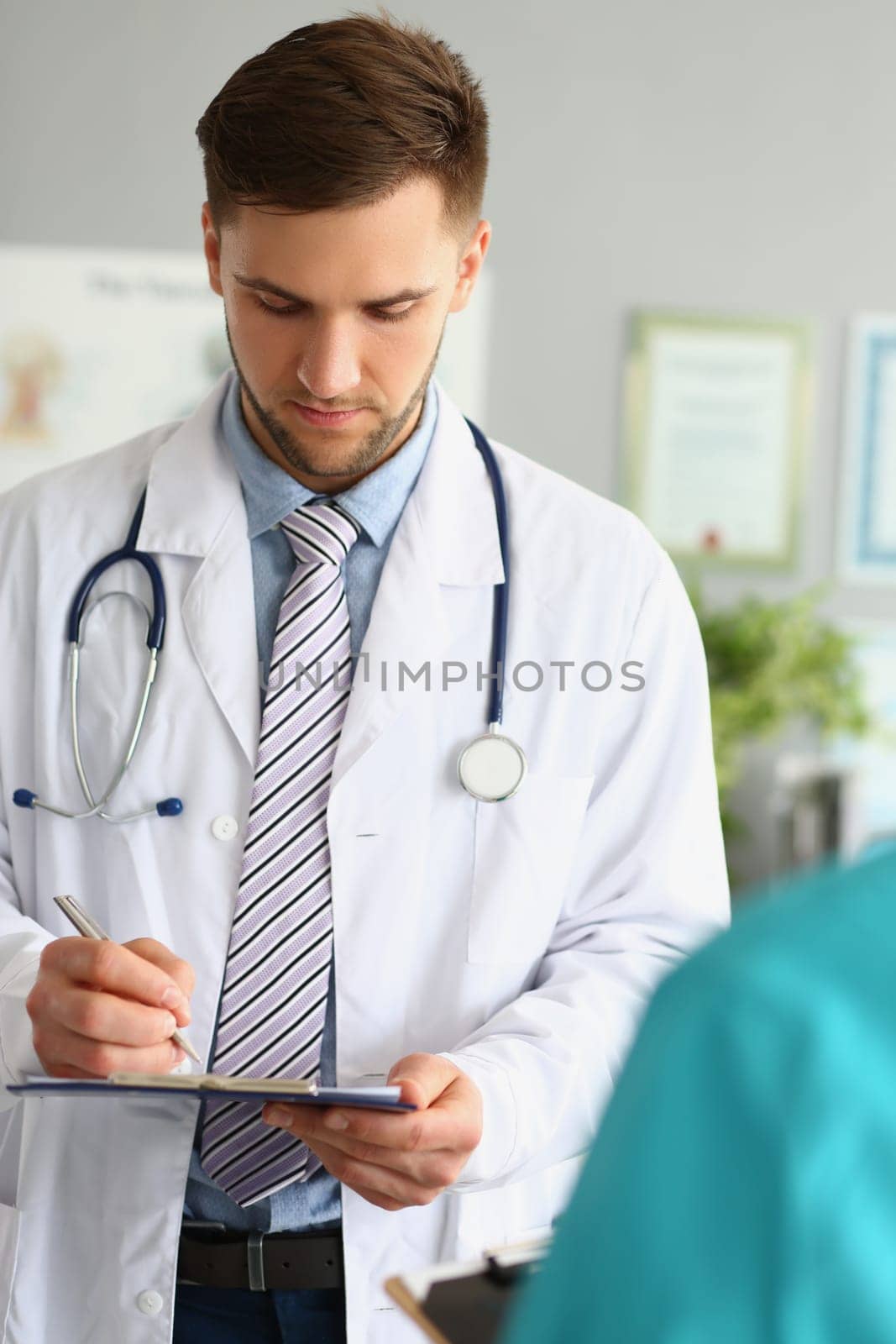 Male doctor filling out patient medical form in clinic. Medina contract and insurance concept