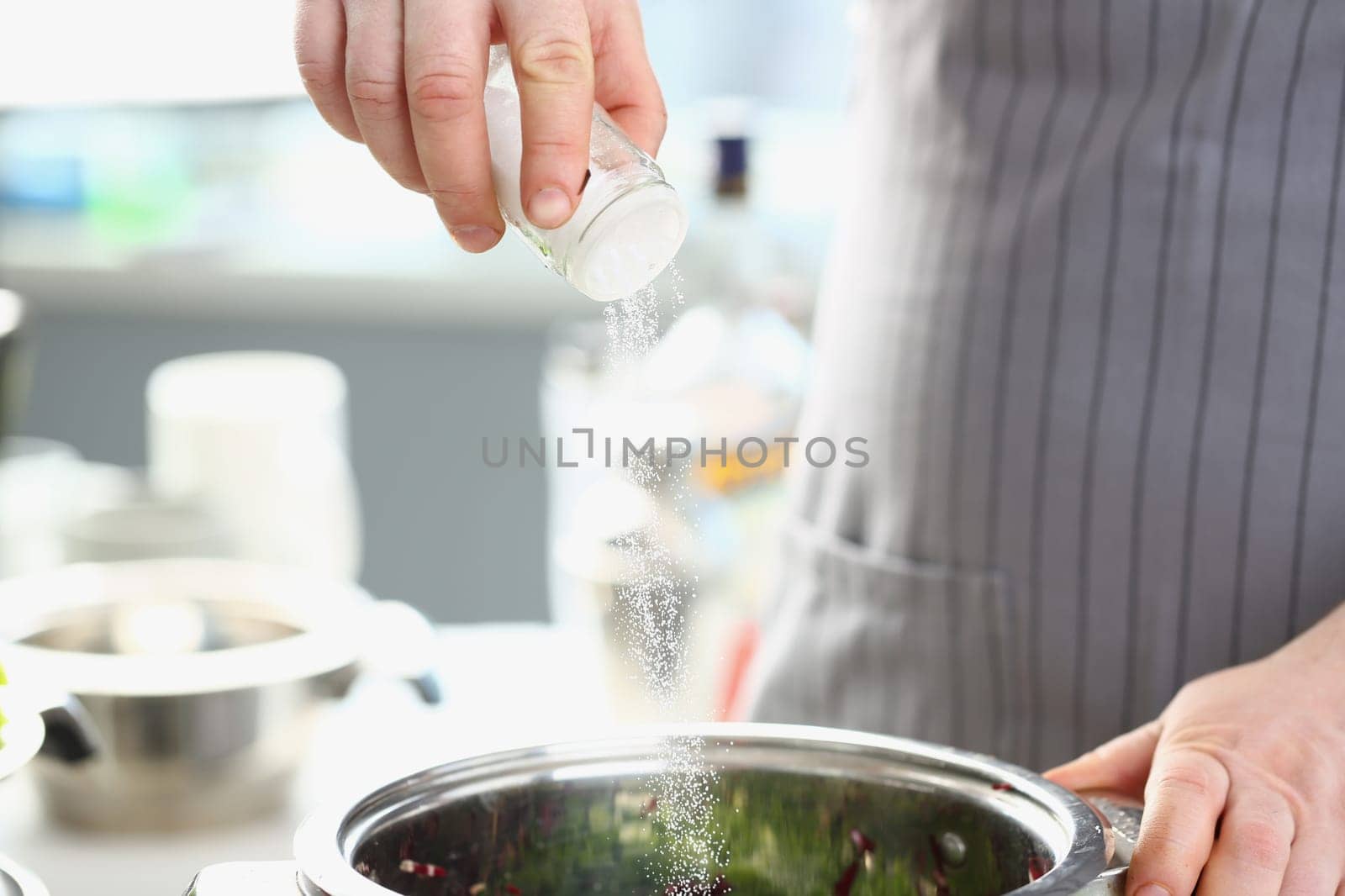 Cook pours salt into pan in kitchen by kuprevich