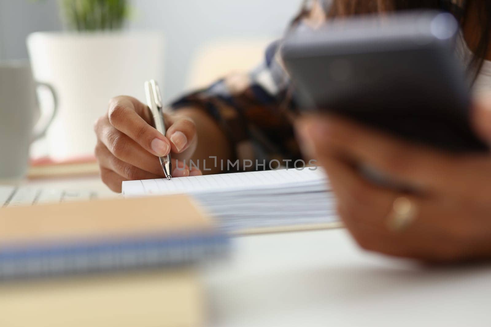 Woman writes in notebook with pen in office and holds smartphone. Mobile applications for business notes