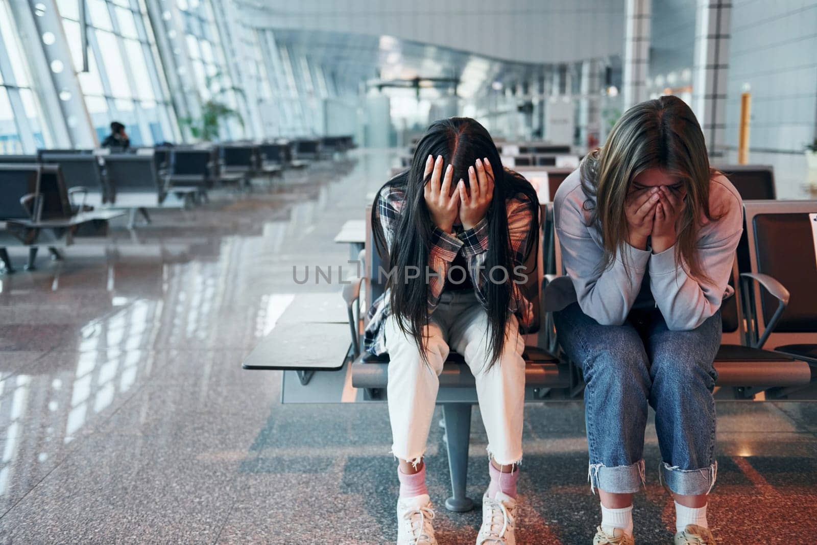 Sad young girl crying with her friend when sitting in the modern airport.