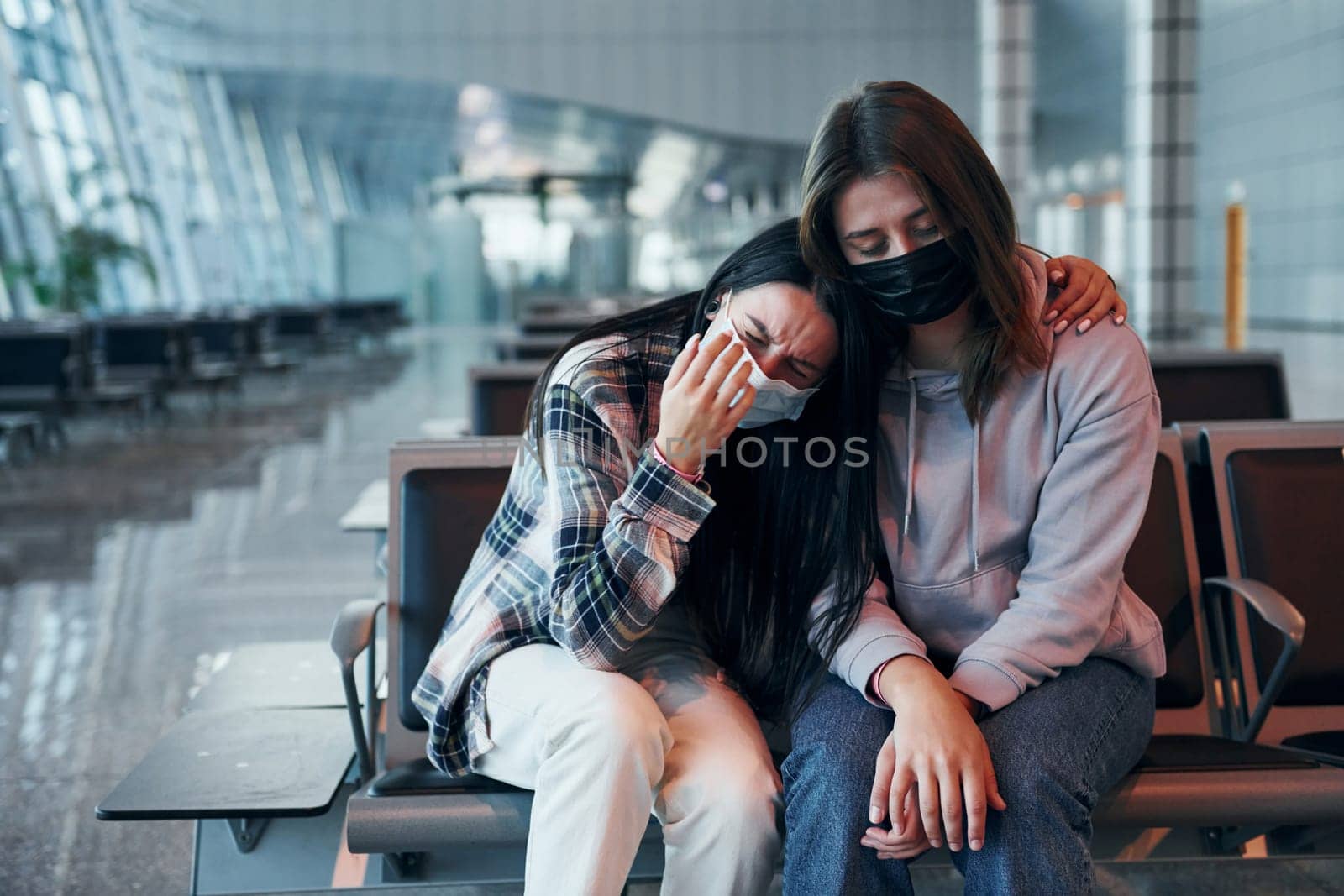 Sad young girl crying with her friend when sitting in the modern airport.