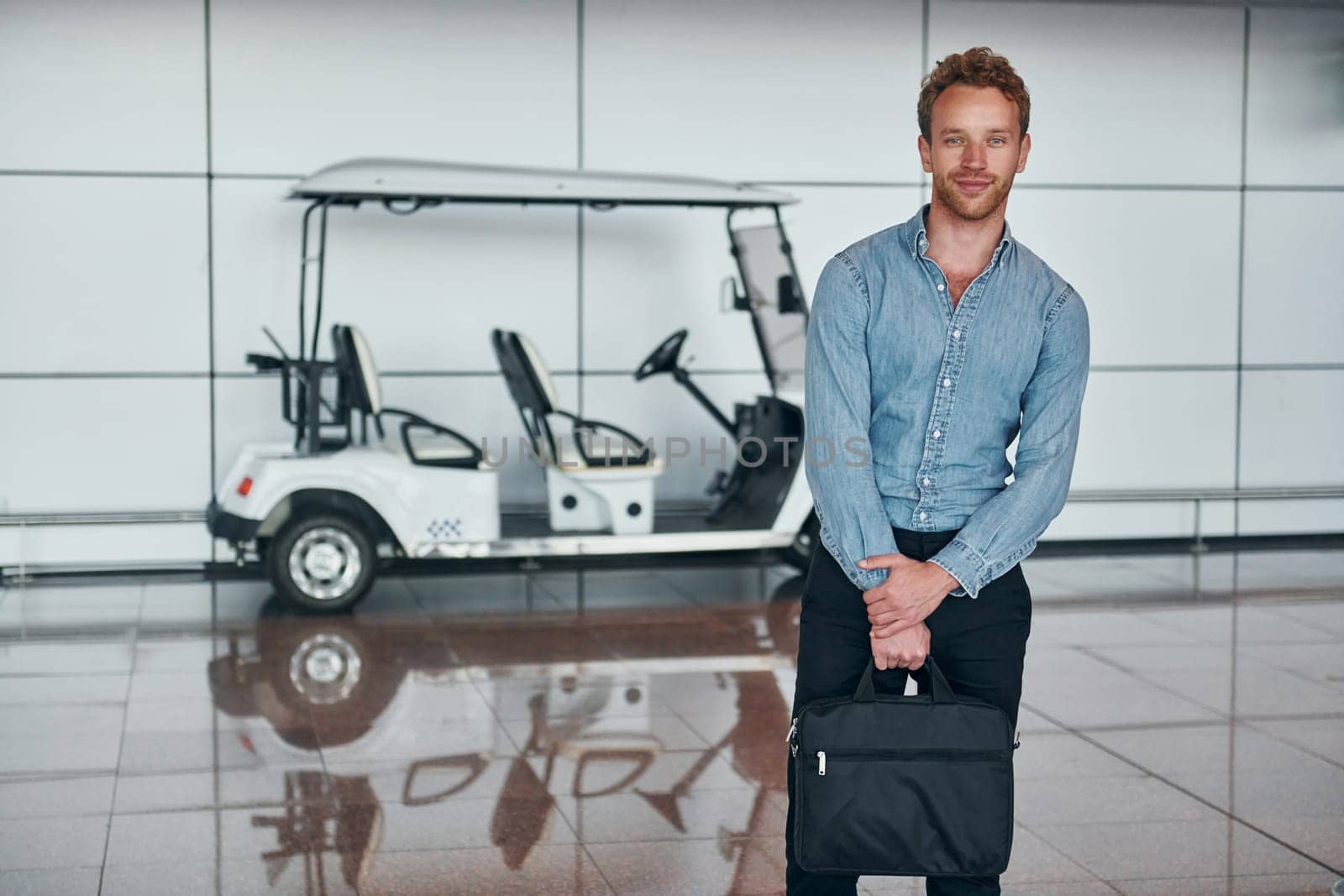 Against vehicle. Young man in formal wear is in modern airport. Conception of vacation.
